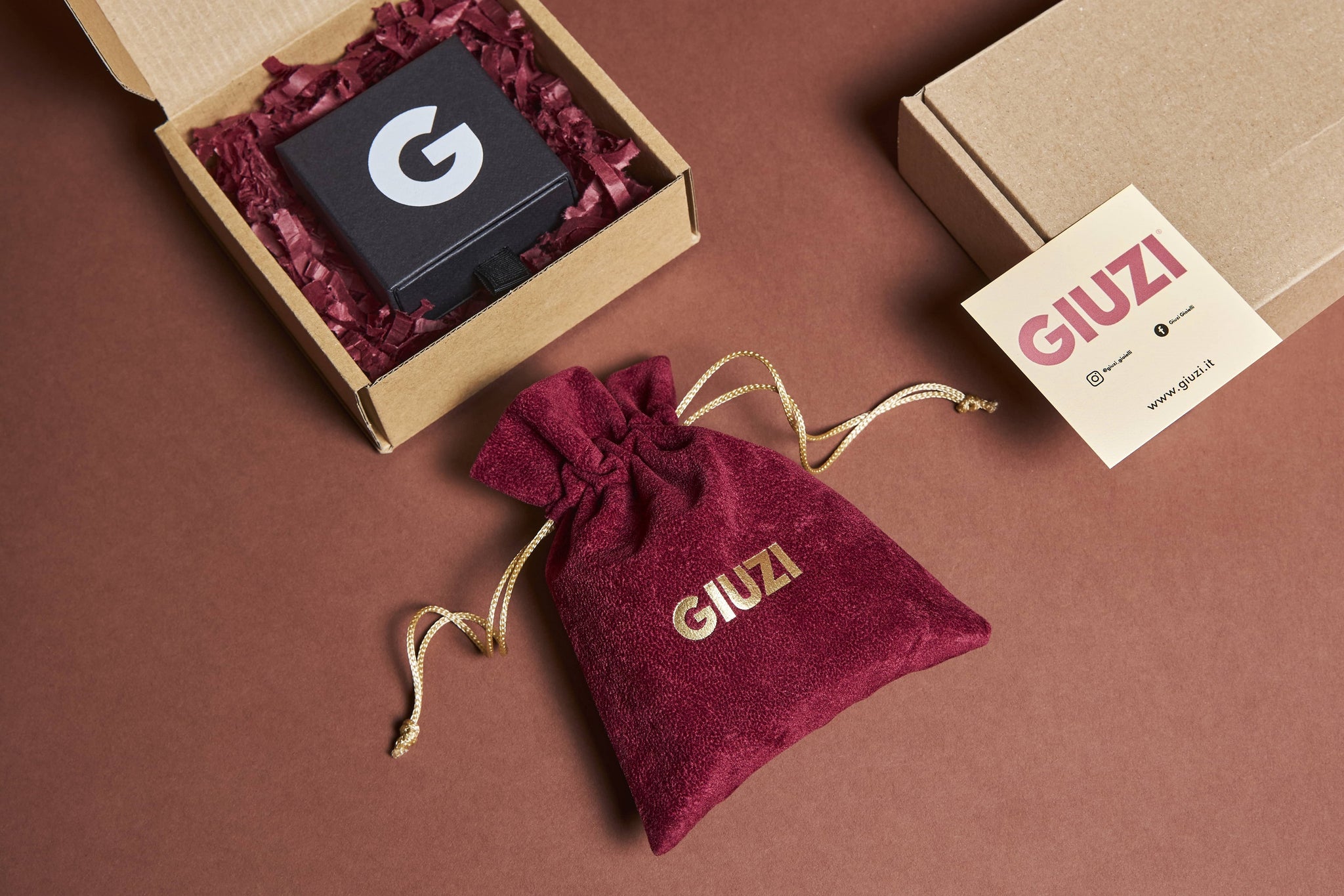 Confezione regalo composta da sacchettino in velluto amaranto con logo GIUZI oro, scatolina nera e tutto contenuto in una scatola di cartone riciclato.